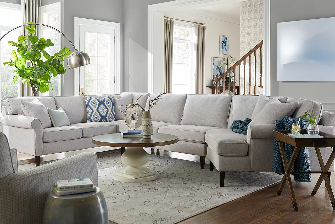 A Jenna sectional in Dove and swivel accent chair in Brio Silver Moon with Rowan Coffee and tray end tables in a room scene.