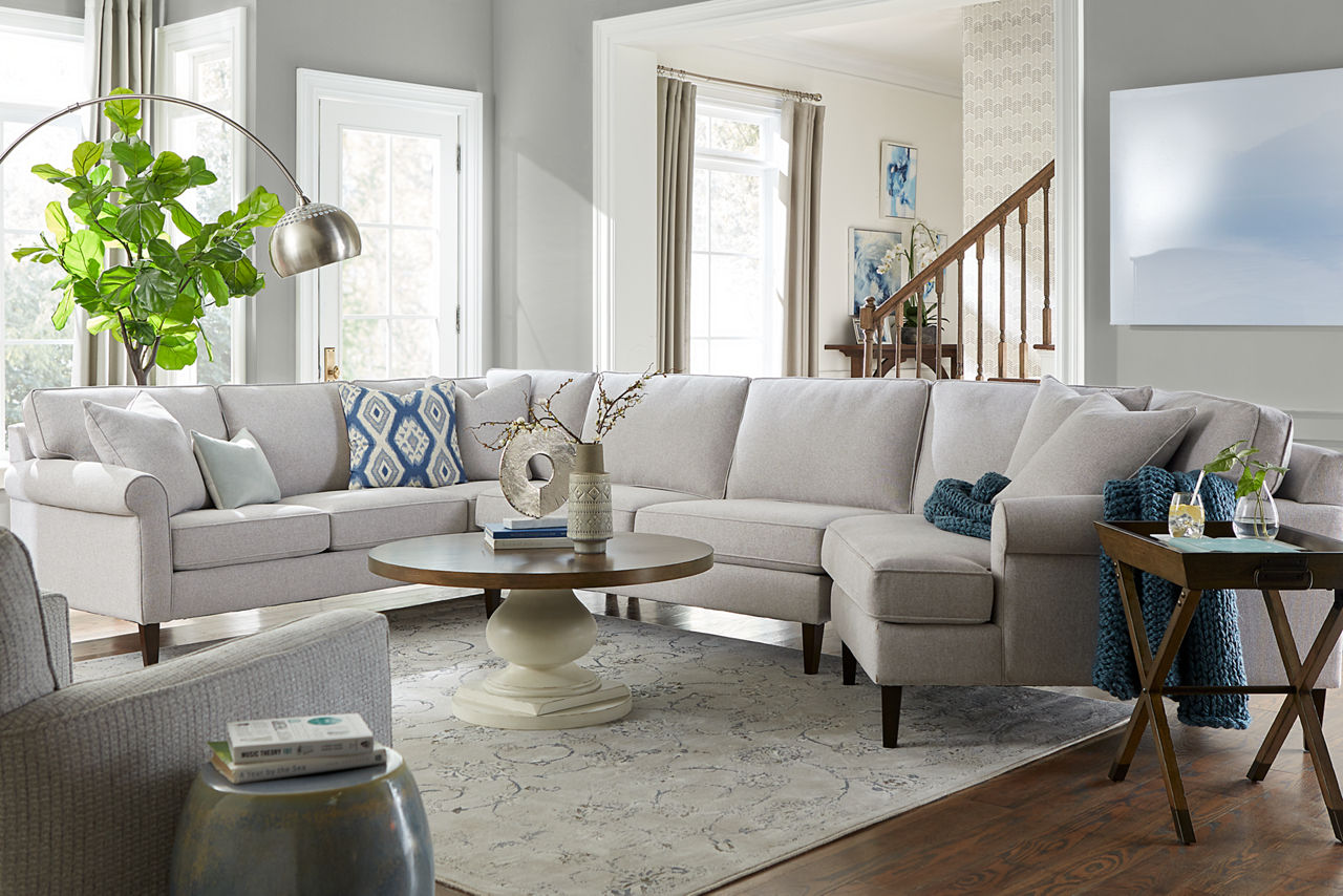 A Jenna sectional in Dove and swivel accent chair in Brio Silver Moon with Rowan Coffee and tray end tables in a room scene.