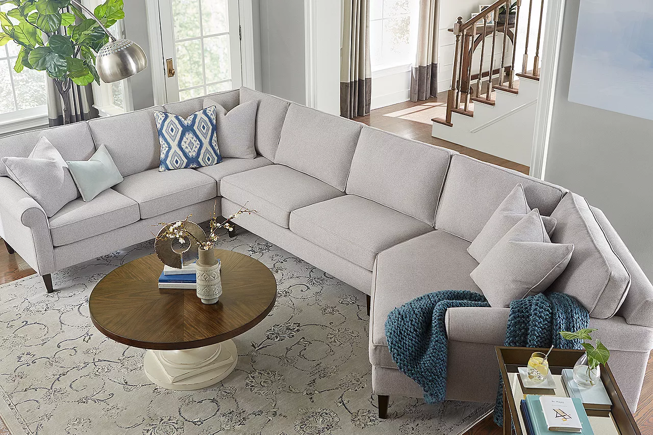 A Jenna sectional in Dove and swivel accent chair in Brio Silver Moon with Rowan Coffee and tray end tables in a room scene.