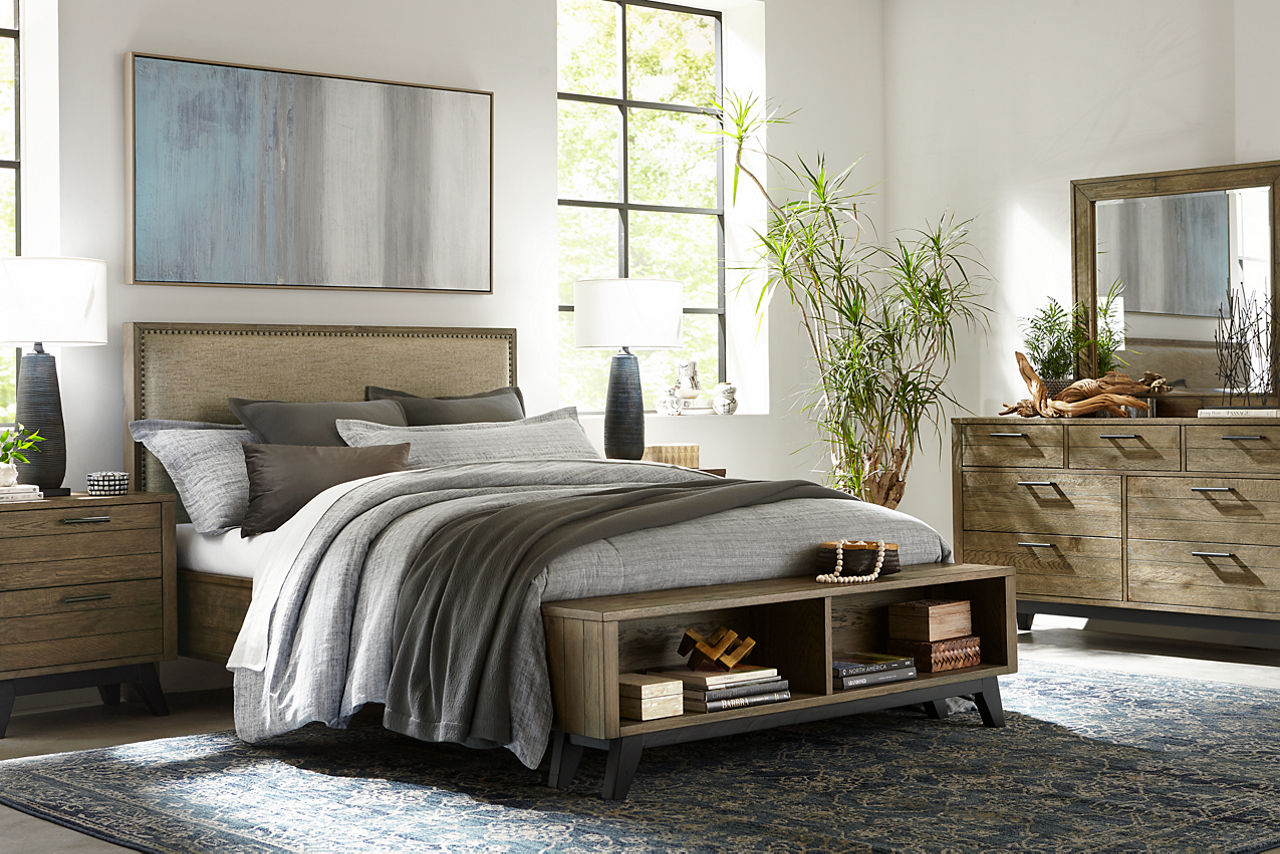 Boulder Creek upholderted bed with a storage foot board, nightstand, and dresser with mirror in Weathered Oak in a room scene.