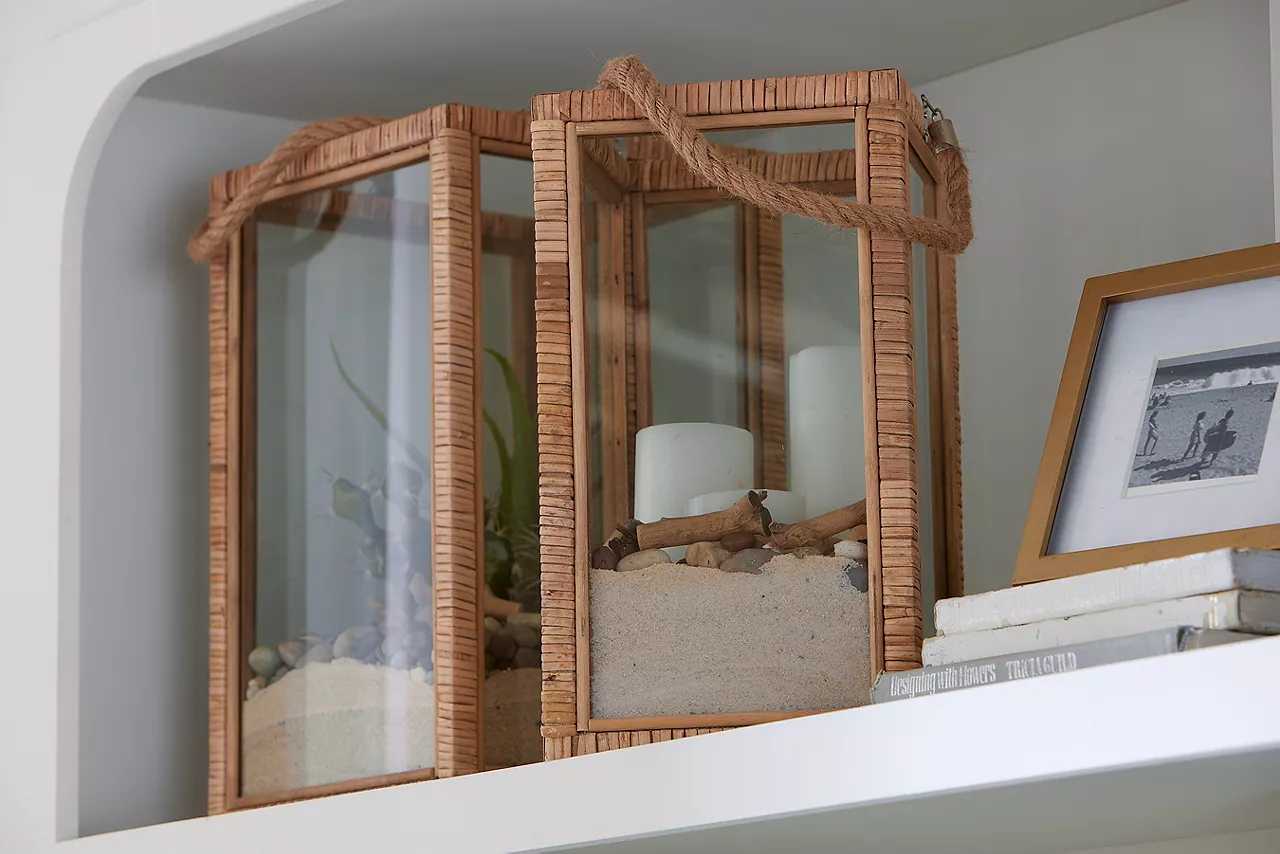 Two glass and wood lantern candleholders on a shelf in a room scene.