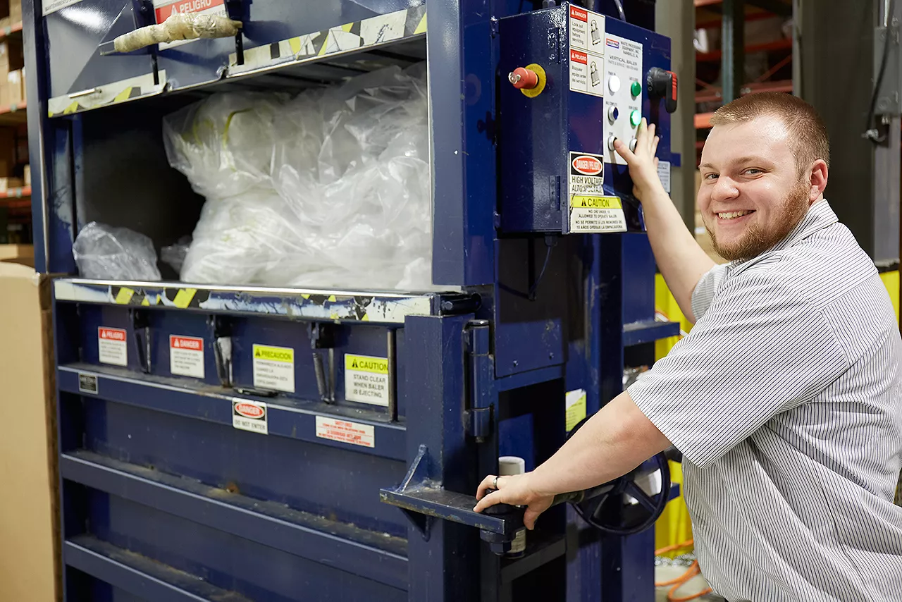 Image of man smiling next to plastic to be recycled